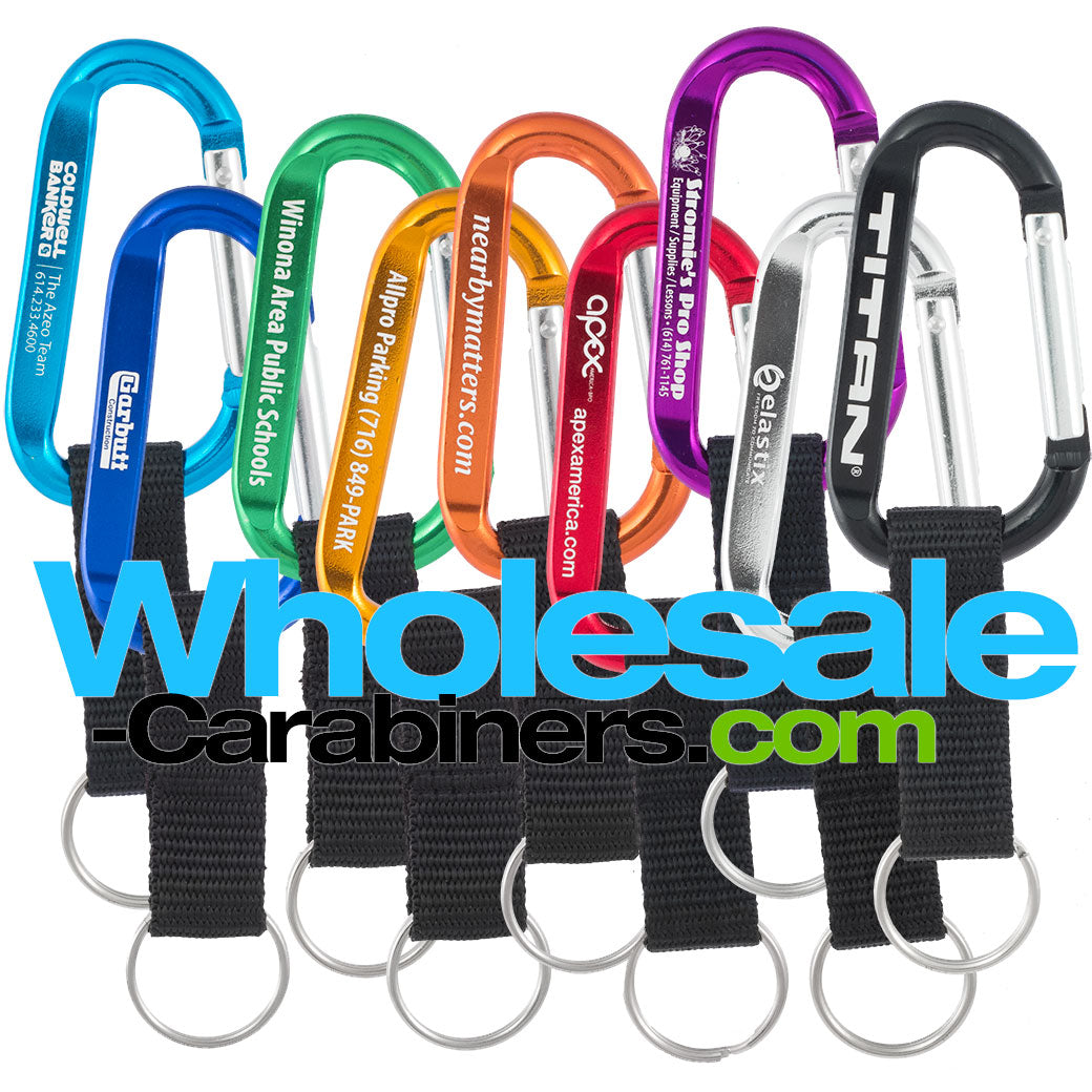 Nine 60mm engraved carabiners, in light blue, dark royal blue, green, gold, orange, red, purple, silver and black, with attached nylon straps with a white background.