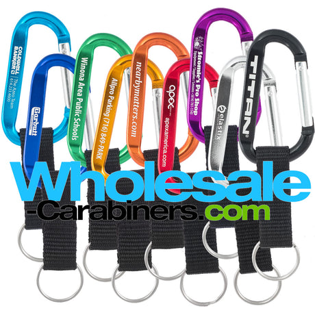 Nine 60mm engraved carabiners, in light blue, dark royal blue, green, gold, orange, red, purple, silver and black, with attached nylon straps with a white background.