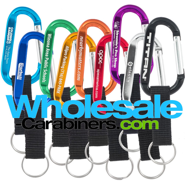 Nine 60mm engraved carabiners, in light blue, dark royal blue, green, gold, orange, red, purple, silver and black, with attached nylon straps with a white background.